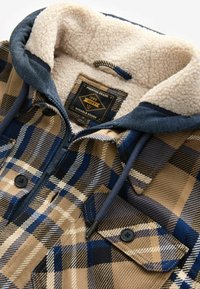 Geruite jas in tan, marineblauw en blauwe kleuren. Zachte fleece voering met een donkere capuchon, ritssluiting en twee voorzakken.