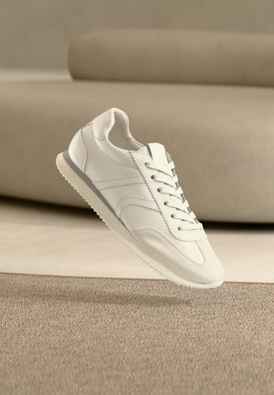 Balti odiniai sportbačiai su lygiu paviršiumi, išlenktu dizainu, tekstūruotais akcentais ir šviesios spalvos guminėmis padomis.