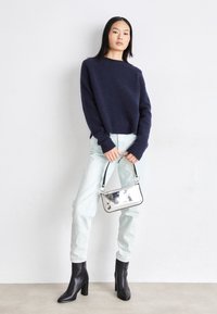 Marineblå genser, lyseblå jeans, svarte hælboots og metallisk sølvveske. Genseren har en strukturert finish og kort design.