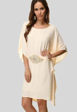 Vestido de longitud a la rodilla, de color crema, con mangas de murciélago y un cinturón decorativo y adornado que presenta acentos multicolores. Textura de tela suave.