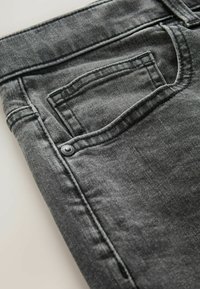 Tumedat hallid teksad, millel on eesmine tasku, nähtav õmblus ja metallne nupudetail. Kangas on peene tekstuuriga.