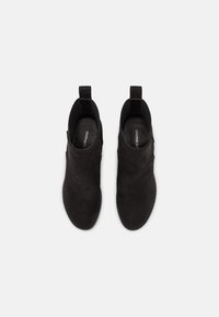 Botines de ante negro con textura suave, punta redondeada y lengüeta en el talón para facilitar su colocación.