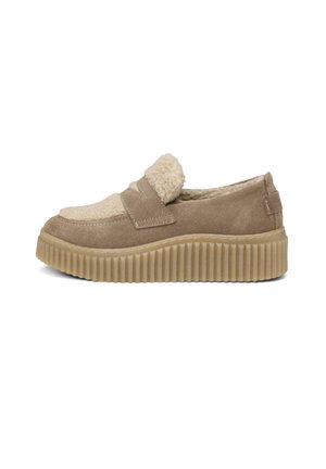 Beige slip-on shoe with a textured suede upper, fleece accents, and a ribbed rubber sole. The design features a rounded toe and cushioned interior.