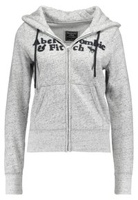 Felpa grigia con zip realizzata in tessuto morbido, dotata di cappuccio con coulisse, tasche frontali e logo stampato nero sul petto.