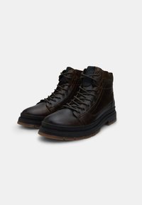 Stivali ankle in pelle marrone con suole in gomma nera, punte rotonde e cuciture a contrasto; presenta occhielli metallici e design con lace-up.