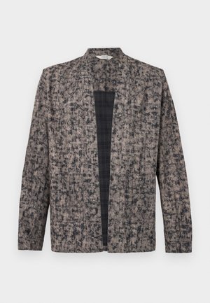 Bunda s dlhými rukávmi, otvorená vpredu, s béžovo-čiernym škvrnitým vzorom a viditeľnou čiernou károvanou podšívkou vo vnútri.