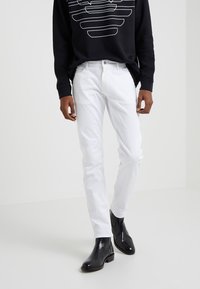 Vita jeans med slim fit, kombinerat med en svart sweatshirt med grafisk design. Modellen bär svarta ankelboots.