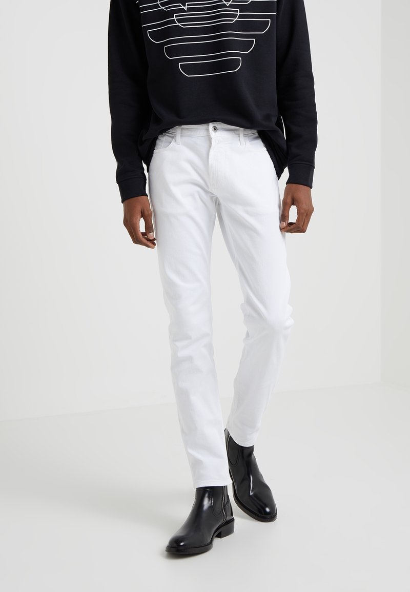 Vita jeans med slim fit, kombinerat med en svart sweatshirt med grafisk design. Modellen bär svarta ankelboots.