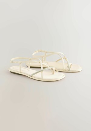 Sandale albe cu barete subțiri, cu talpă plată, având un accent argintiu strălucitor. Material moale, design minimalist și curele reglabile pentru glezne.