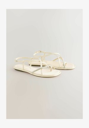 Sandale albe cu barete subțiri, cu talpă plată, având un accent argintiu strălucitor. Material moale, design minimalist și curele reglabile pentru glezne.