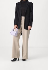Schwarzes Blazer, durchsichtiges schwarzes Top, beiger weiter Hosenanzug, schwarze spitze Pumps und eine kleine lavendelfarbene Handtasche mit einem Griffdetail.