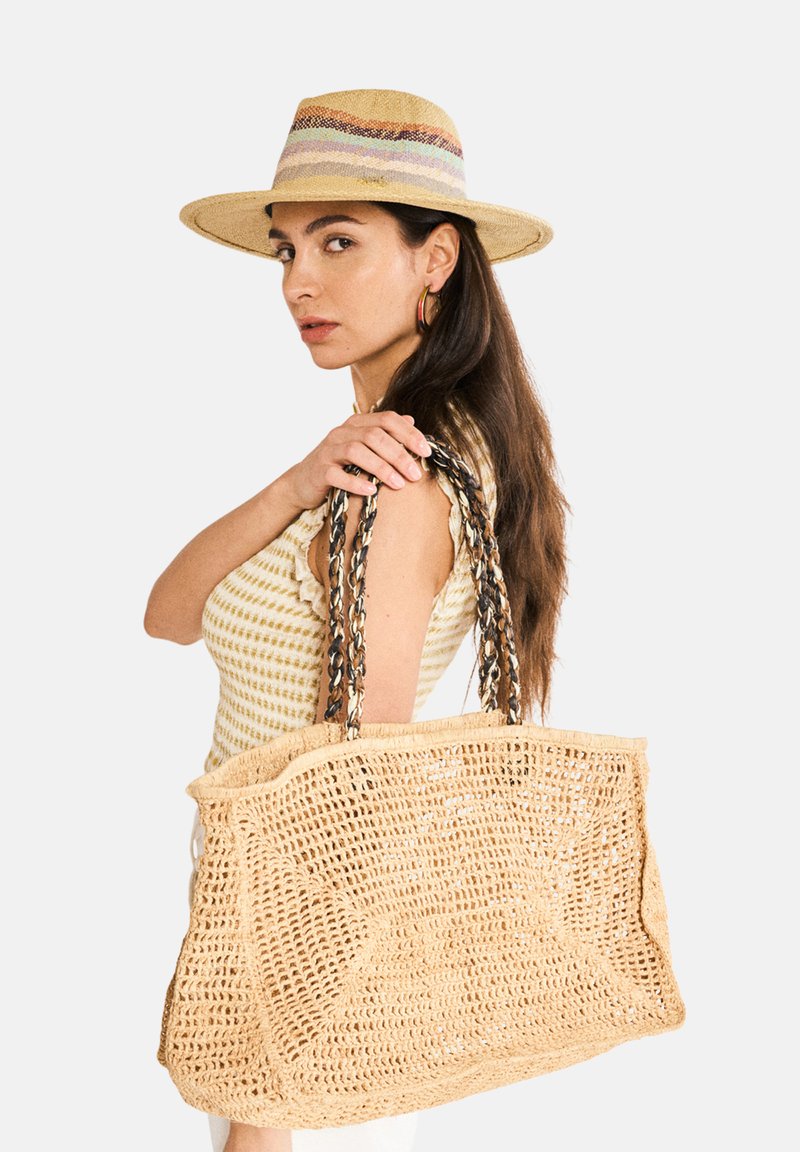 Iso kankuri virkattu olkalaukku, jossa on kaksinkertaiset punotut kahvat ja tekstuuri. Neutraali beige väri ja orgaaninen muoto.