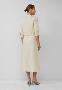 Crème linnen jurk met een cropped, geborduurd jasje. De jurk heeft driekwart mouwen en een getailleerde taille, met een vloeiende rok en een ritssluiting aan de achterkant.