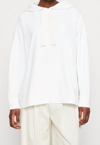 Felpa bianca con cappuccio e coulisse, vestibilità comoda e maniche lunghe. Tessuto morbido con una texture liscia e senza motivi visibili.