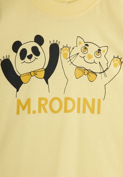 Gul bomull T-skjorte med en svart panda og hvit katt med gule aksenter, begge iført sløyfer, over teksten "M. RODINI."