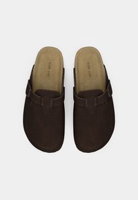 Καφετί σουέτ παπούτσια τύπου κλογκ με επίπεδη σόλα, που διαθέτουν αγκράφα στο λουρί και επένδυση εσωτερικά για άνεση.