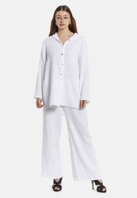 Wit, textuur loungewear-set bestaande uit een langemouwen overdhemden en wijde broek, gecombineerd met zwarte hoge hakken sandalen.