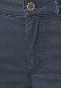 Navy blue denim trousers with a smooth texture, featuring a front pocket and a metal button with engraved brand name.