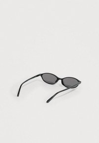 Μαύρα γυαλιά ηλίου cat-eye με σκουρόχρωμους φακούς, γυαλιστερό πλαίσιο από μαύρο πλαστικό και καμπυλωτούς βραχίονες. Μινιμαλιστικός σχεδιασμός με λεία υφή.