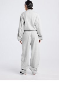 Harmaa lyhyt collegepaita ja siihen sopivat collegehousut, valmistettu pehmeästä kankaasta. Löysä istuvuus, joustava vyötärönauha ja resorit hihansuissa. Mustat kengät näkyvissä.