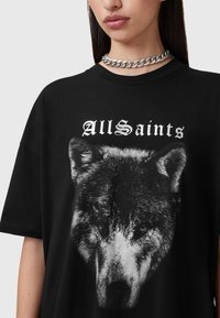 Mustavilla puuvillapaita, jossa on harmaasävyinen susigrafiikka, ja "AllSaints" -teksti painettuna valkoisella goottikirjaimilla ylle. Lyhyet hihat ja rento istuvuus.