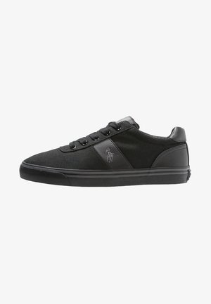 Basket basse noire avec fermeture à lacets à l’avant, panneaux en tissu et en cuir, et un logo cheval brodé sur le côté.