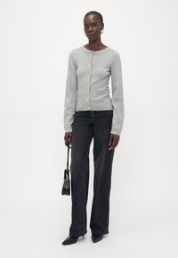 Gray knitted cardigan with round neckline, featuring five buttons, a front pocket, and ribbed cuffs, paired with black wide-leg jeans and a small handbag.