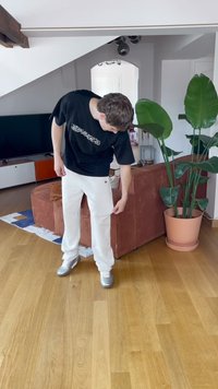 Hvide løstsiddende bukser med en dekorativ side-detail, parret med en sort t-shirt med korte ærmer, der har et grafisk design, sat i et lyst rum.