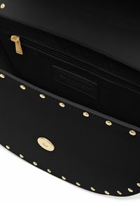 Schwarze Lederhandtasche Innenraum mit goldenen Nieten am Rand, ausgestattet mit einem Reißverschlussfach und einer glatten Textur. Details aus goldfarbenem Metall sind vorhanden.