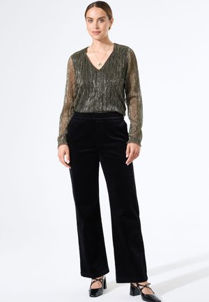 Glanzende groene blouse met lange mouwen en een V-hals, gecombineerd met hoge zwarte corduroy broek en zwarte blokhak schoenen.