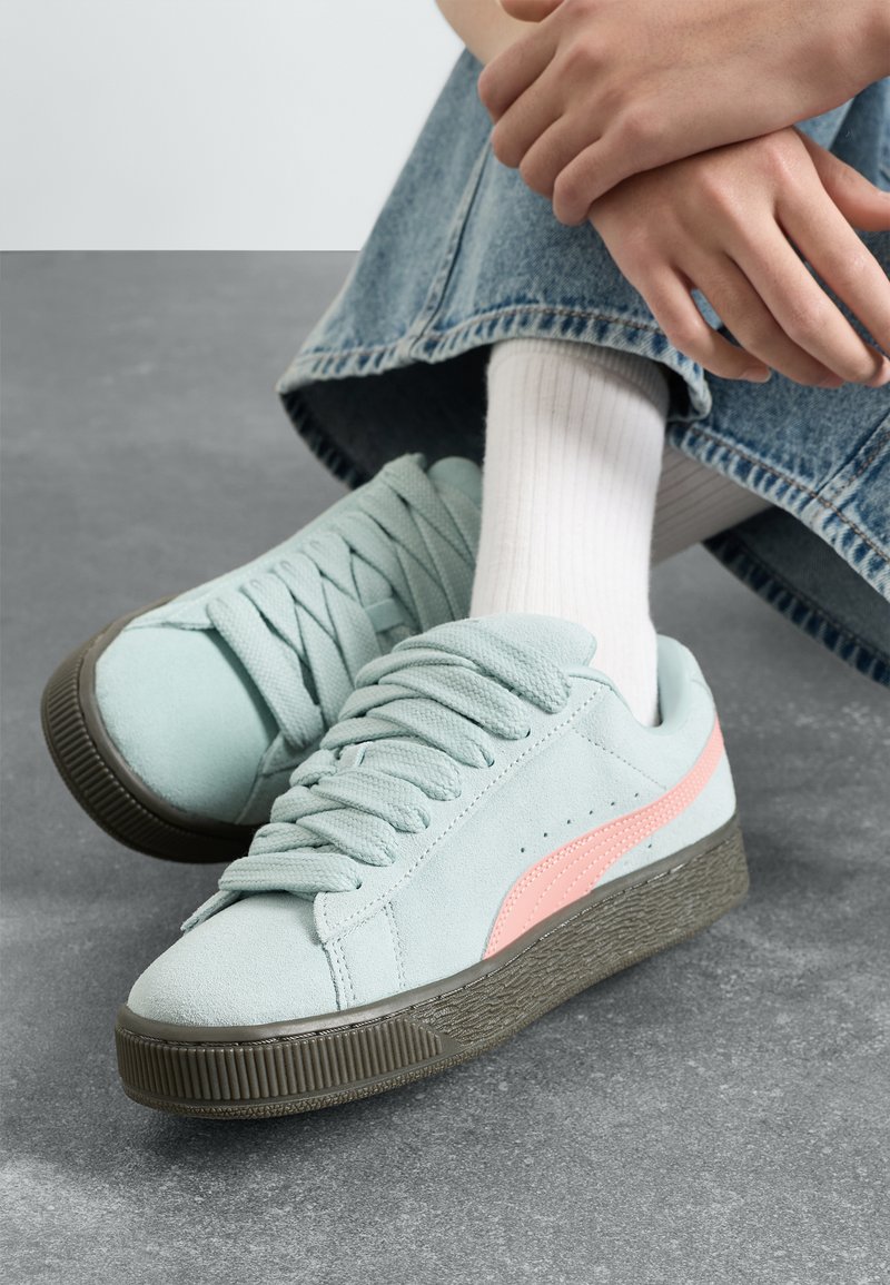 Svijetloplavi sneakersi od suedea s ružičastim akcentima, teksturirana siva gumena potplata i ravne vezice. Nosi se s bijelim rebrastim čarapama i trapericama.