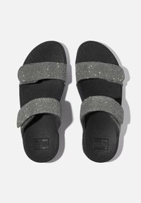 Zwarte sandalen met twee brede, sprankelende grijze banden en een teksurierte voetbed. De zool is plat, met een merkembleem op één sandaal.