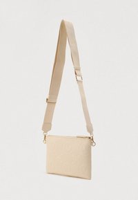 Bolso bandolera beige con correa ajustable, cierre de metal dorado y patrones circulares con logo en relieve sobre tela texturizada.