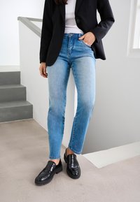 Lichtblauwe spijkerbroek met een rechte snit en vervaagde textuur, gecombineerd met een zwart colbert en zwarte instap loafers.