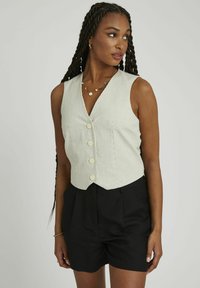 Gilet rayé vert clair avec un col en V, cinq boutons et un design court, associé à un short noir ajusté. Texture lisse, sans motifs.