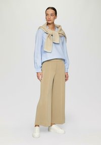 Blouse rayée bleu clair avec des manches bouffantes, pantalon large beige, et baskets blanches. Un foulard beige est drapé sur les épaules.