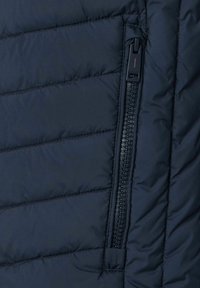 Marine gewatteerde jassectie met een gesloten zijrits. De stof heeft een gladde textuur met horizontale gestikte patronen.