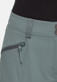 Un short de randonnée bleu clair avec un tissu texturé, une poche latérale zippée et deux boutons métalliques à la taille pour le fermer.
