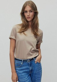 Beige t-paita lyhyillä hihoilla, joissa on käänteet, sileä tekstuuri, yhdistetty sinisiin farkkuihin, joissa on musta vyö ja hienovaraisia metalliosia.