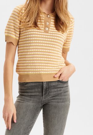 Femme portant un top en maille à manches courtes beige et rose rayé avec des boutons floraux, associé à un jean gris délavé taille haute.