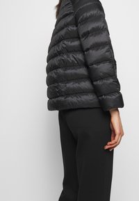 Sort pufferjakke med en quiltet design, der har høj krave og korte ærmer. Glat, blankt stof med en tætsiddende silhuet.