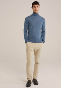 Blå stickad polotröja i kombination med beige byxor. Outfitten har en kroppsnära design och en slät textur, kompletterad av bruna skor.