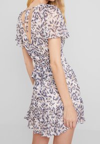 Šaty s krátkým rukávem vyrobené z lehké, vzorované tkaniny. Mají výstřih do V na zádech se stuhou, volánkový lem a stažený pas pro přiléhavý vzhled.