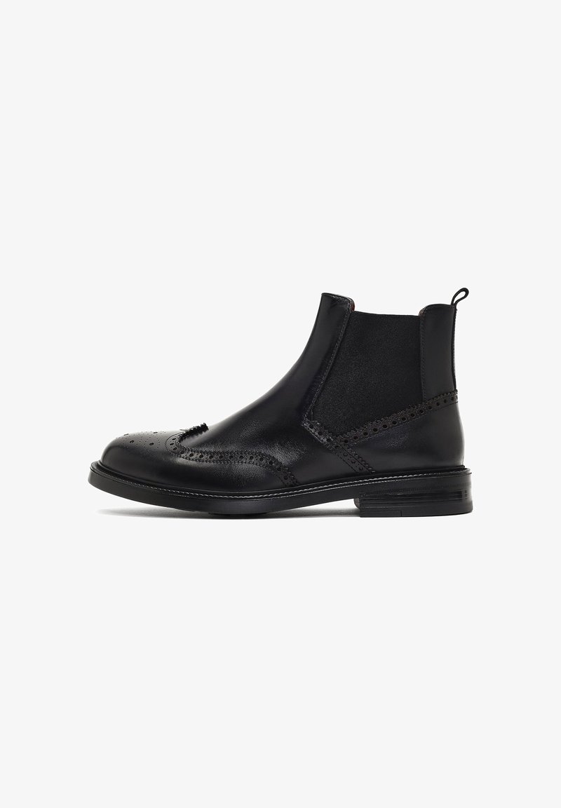 Botas Chelsea de cuero negro con acabado suave, detalles de perforaciones tipo brogue, paneles elásticos en los laterales y puntera redondeada. Suela plana.