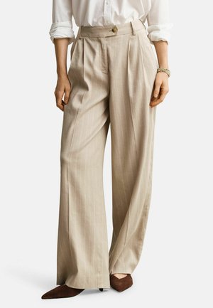 Beige Hosen mit weitem Bein und Nadelstreifen, kombiniert mit einem weißen Hemd und braunen spitz zulaufenden Absätzen, gezeigt von der Taille bis zu den Füßen.