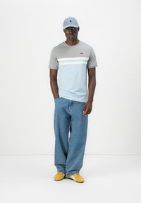 Light blue and gray striped t-shirt, loose blue denim jeans, and yellow sneakers. Accompanied by a blue cap with a logo.
