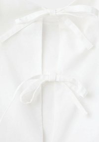 Deux liens en tissu blanc attachés en nœuds simples sur un vêtement blanc avec une couture centrale.