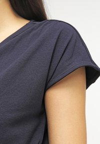 Camiseta de color azul marino con mangas cortas y enrolladas, hecha de suave algodón. Diseño simple con un ligero estiramiento y un ajuste holgado.