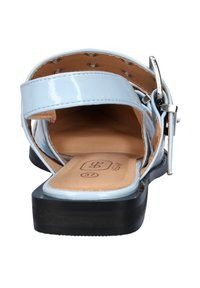 Himmelblaue vegane Sandalen mit glänzender Oberfläche, offener Rückseite und verstellbarem Schnallenriemen. Verfügt über eine flache schwarze Sohle und eine beige Innensohle.