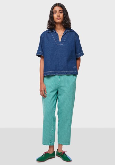 Pullover in denim a maniche corte con scollatura a V, abbinato a pantaloni a righe verdi e bianche in vestibilità rilassata e scarpe verdi con dettagli blu.